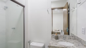 A bathroom with a glass shower enclosure, a toilet, a sink with a marble countertop, and a mirror reflecting a towel rack and a door. - Apt With Pool View, Mins From the sea Vll0001 (Maraú)