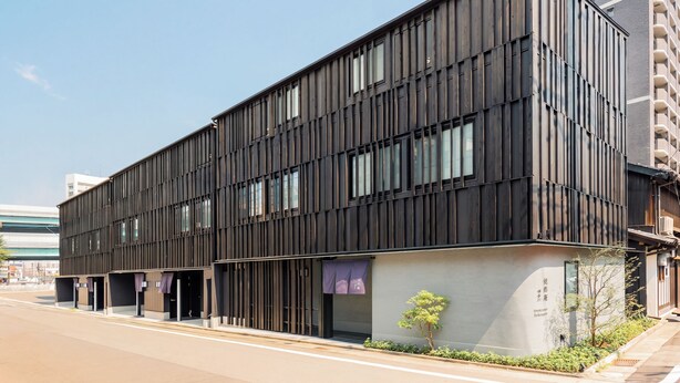 Un edificio moderno con fachada plana, ventanas amplias y un pequeño árbol en primer plano.