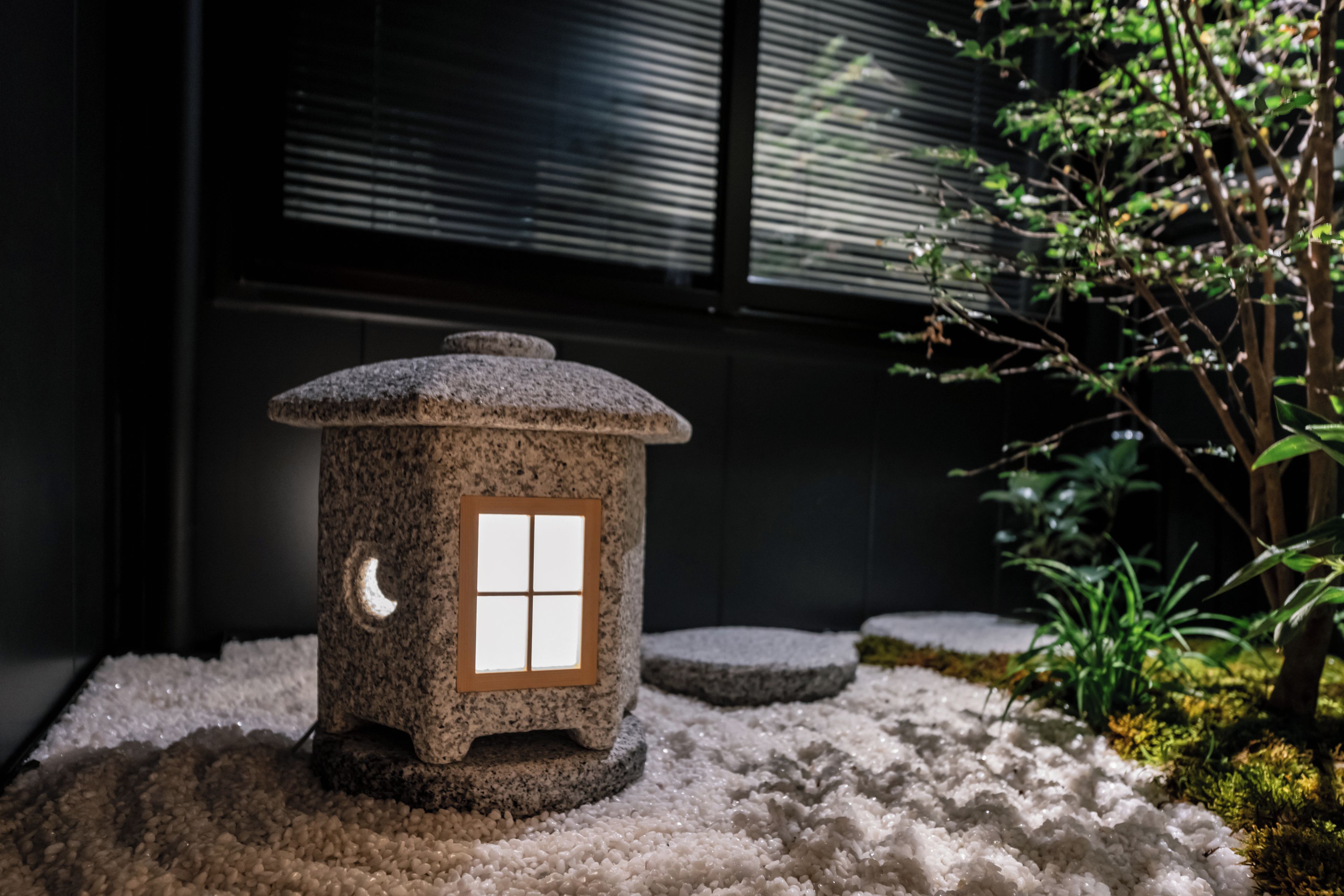 Un farol de piedra con una ventana, sobre una superficie rugosa con musgo y plantas.