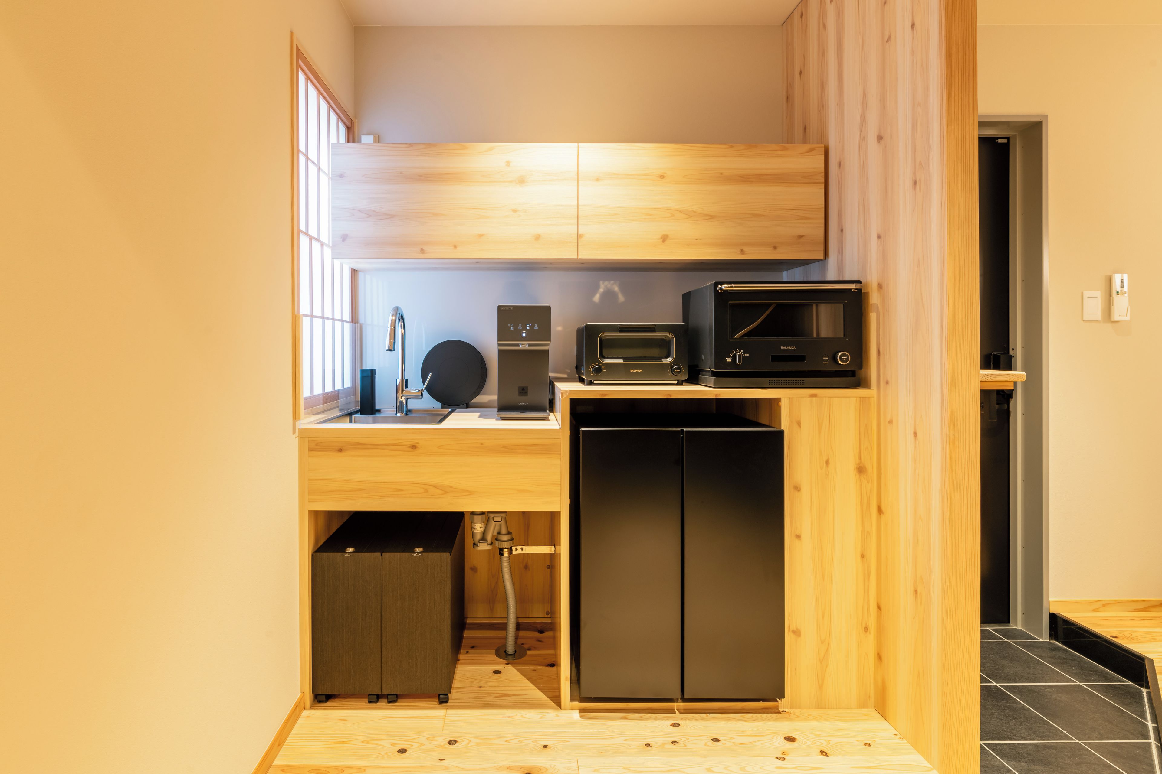 Una cocina compacta con microondas integrado, tostadora y lavavajillas, que presenta armarios de madera y un lavamanos pequeño.
