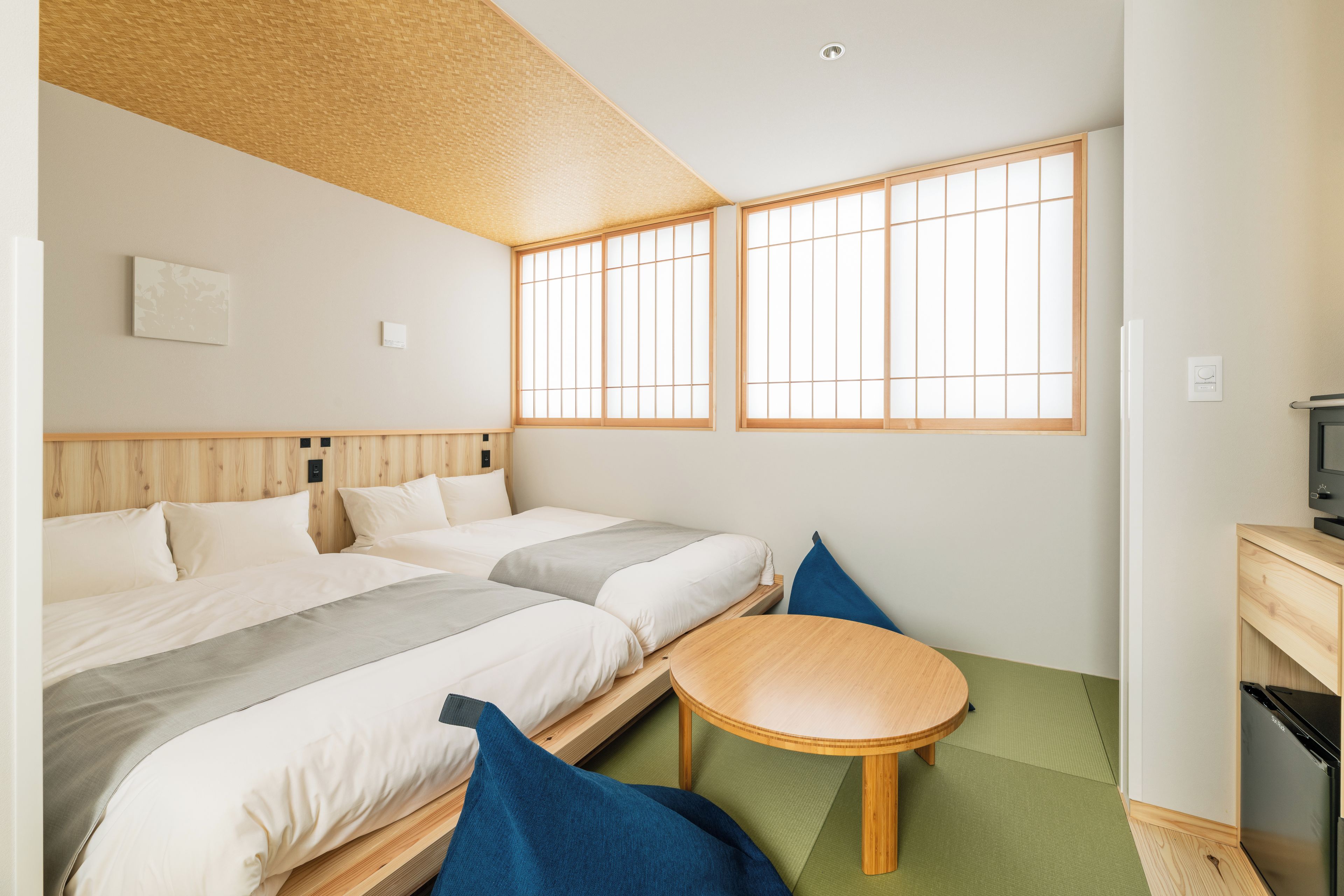 A hotel room with two beds, a small table, a TV, and a view through the windows.