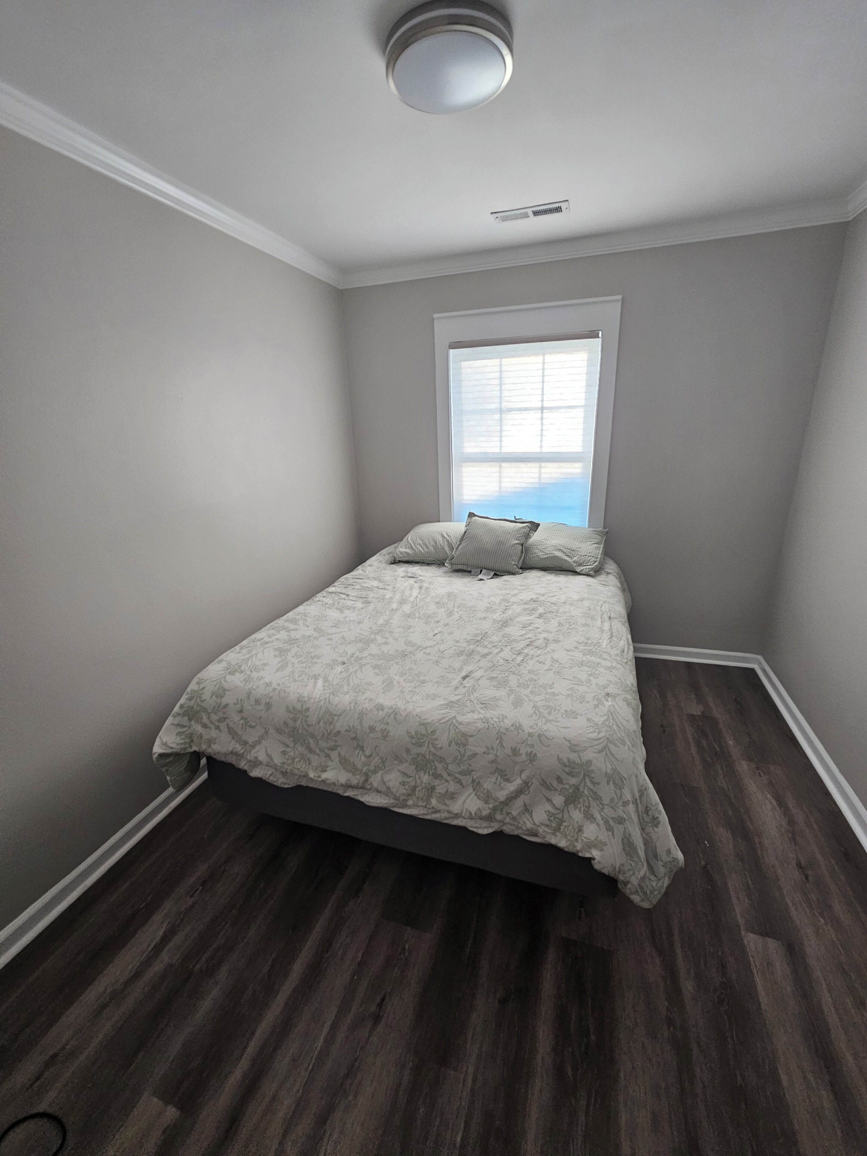 Un dormitorio con cama, ventana y lámpara en el techo.