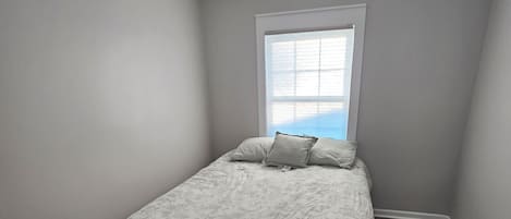 Un dormitorio con cama, ventana y lámpara en el techo.