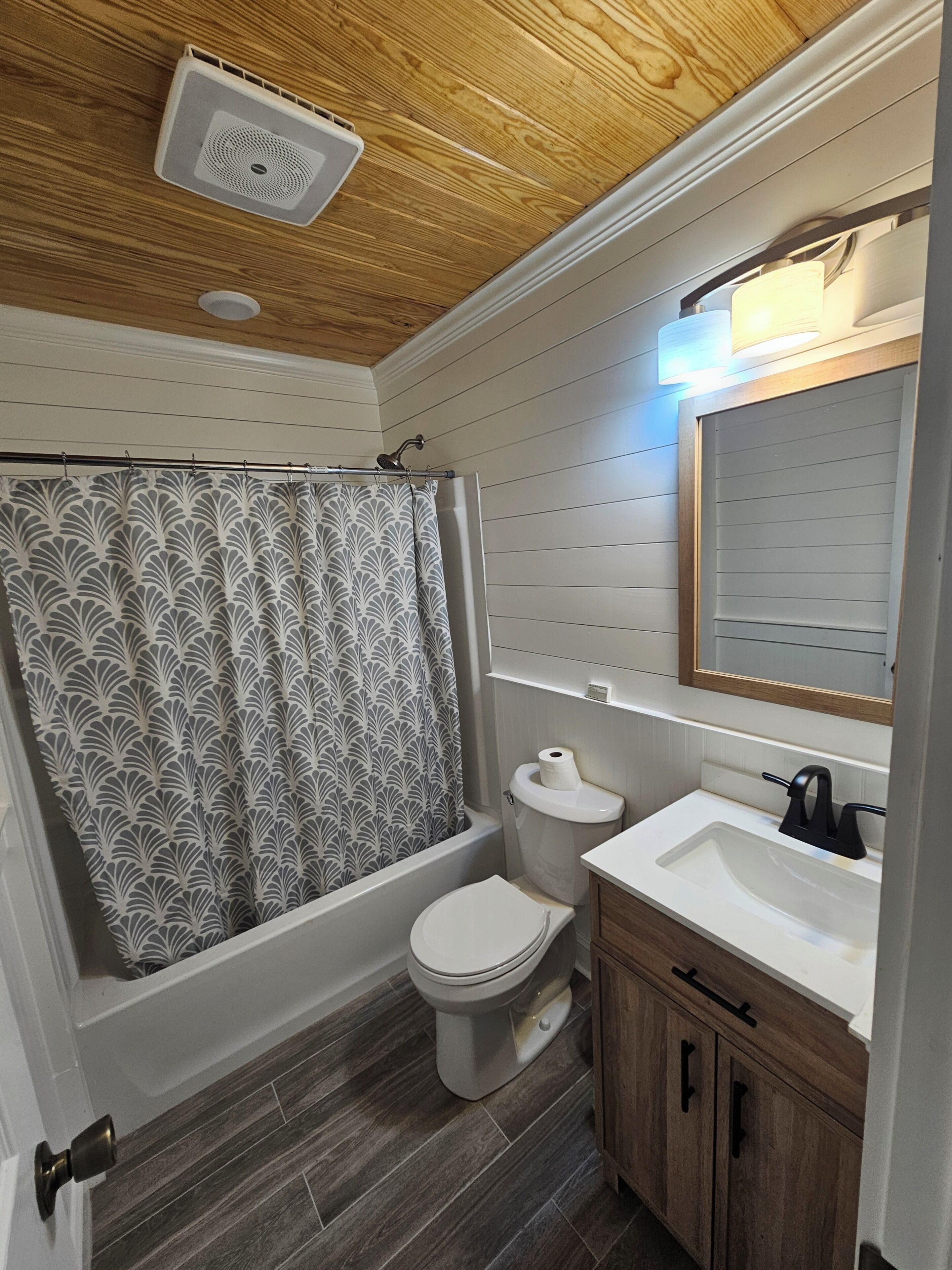 A bathroom with a shower, toilet, sink, and wooden ceiling.