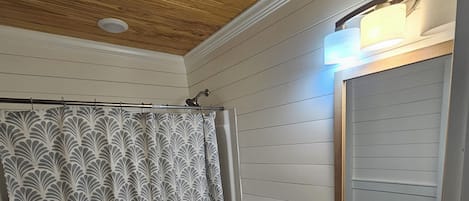 Une salle de bain avec douche, toilettes, lavabo et plafond en bois.