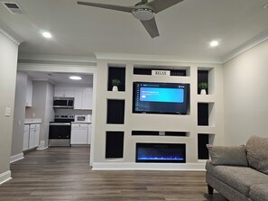 A modern living room with a flat-screen TV mounted on a wall, a ceiling fan, and a fireplace.