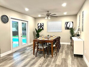 A dining area with a wooden table, chairs, a ceiling fan, and a view of a swimming pool through glass doors.