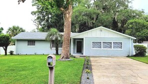 A single-story house with a garage, a driveway, and a parking meter in the foreground.