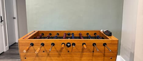A wooden foosball table in a room with a wooden floor and light green walls.