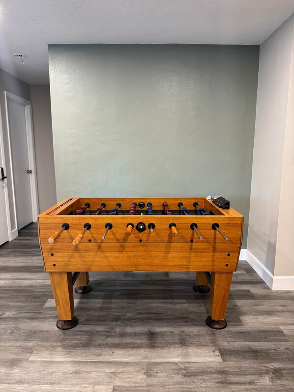 A wooden foosball table in a room with a wooden floor and light green walls.