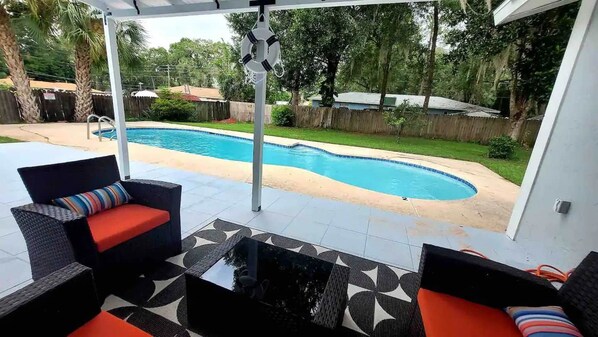 A covered patio area with a pool, outdoor furniture, and a view of the backyard.