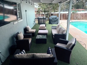An outdoor patio with wicker furniture, a barbecue grill, and a pool.