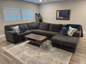 A living room with a sectional sofa, a coffee table, patterned rug, and a framed mirror on the wall.
