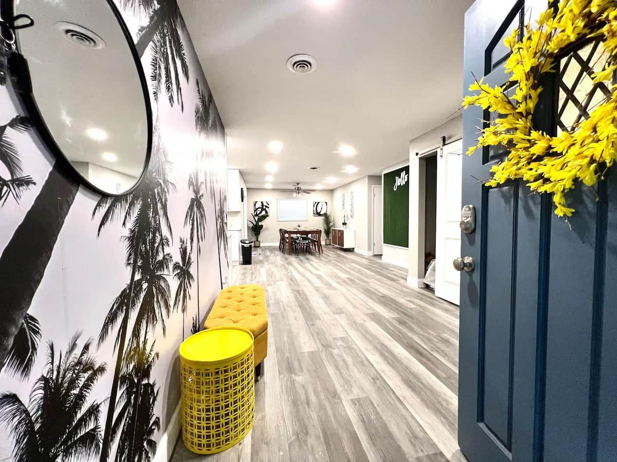 A hallway with a wooden floor, a bench, a mirror, and a door with a plant decoration.