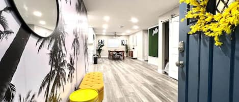 A hallway with a wooden floor, a bench, a mirror, and a door with a plant decoration.