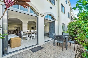 A modern outdoor patio with a dining area, a wicker bench, and a small table. - Mango Resort 2 Bedroom Pool Access 11 (Palm Cove)