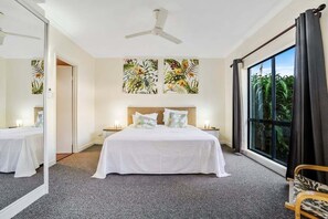 A hotel room with a bed, a ceiling fan, a large window with curtains, and artwork on the wall. - Mango Resort 2 Bedroom Pool Access 11 (Palm Cove)