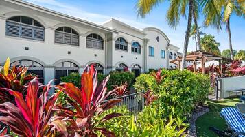A hotel with a white facade, arched windows, and a well-maintained garden with tropical plants.