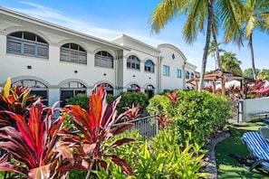 A hotel with a white facade, arched windows, and a well-maintained garden with tropical plants. - Mango Resort 11 | 2 Bedroom Pool Access Apartment (Palm Cove)