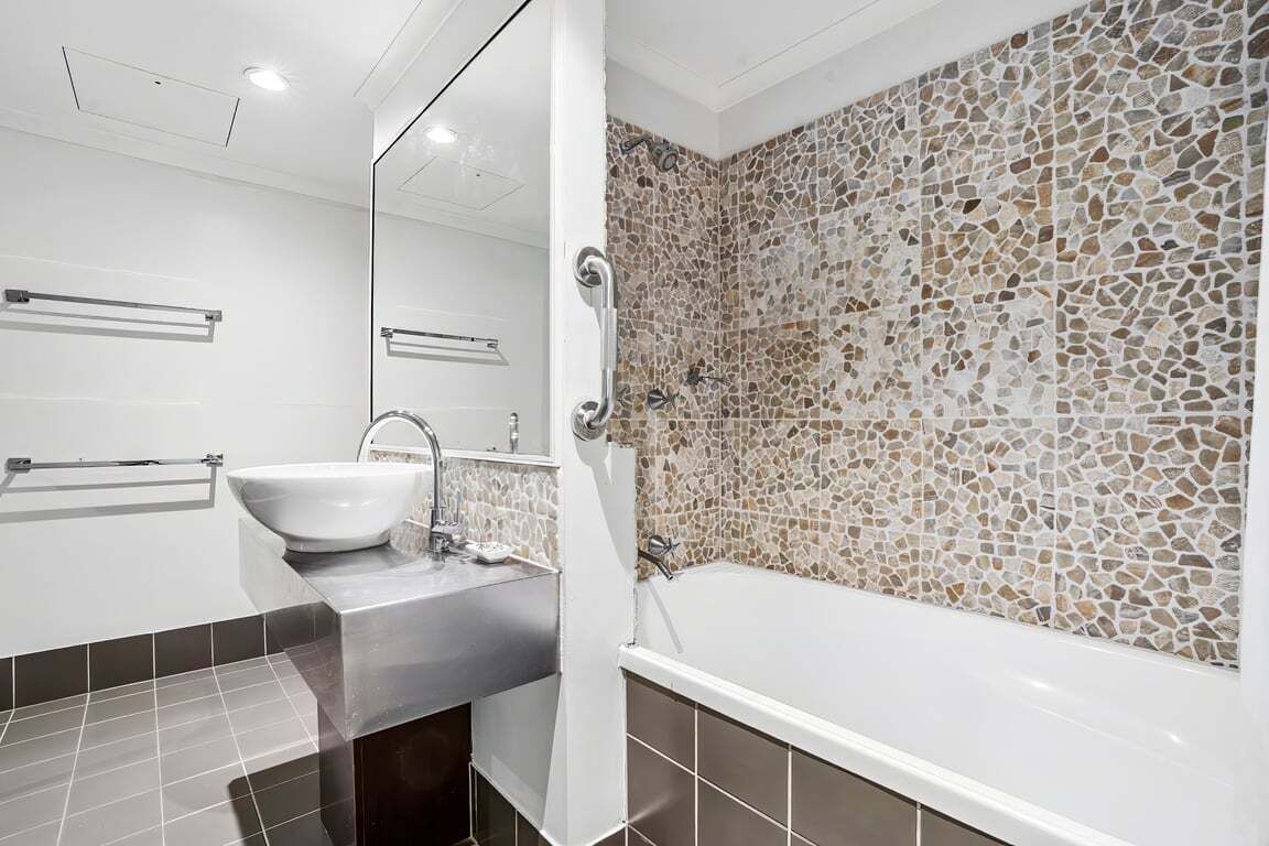 A modern bathroom with a white sink, a bathtub, and a mosaic wall.