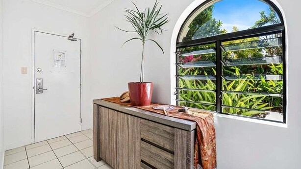 Una habitació amb una porta blanca, un armari de fusta, una planta en test i una finestra que dona a un espai verd.