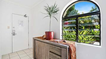 A room with a white door, a wooden cabinet, a potted plant, and a window with a view of greenery.