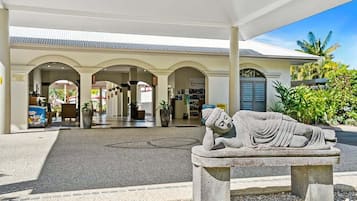A stone statue of a reclining figure in a courtyard with a covered walkway and a building in the background.