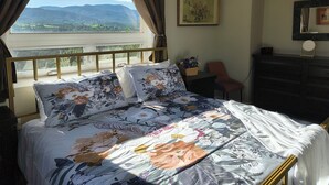 Ein Hotelzimmer mit einem Bett, einem Sessel, einem Schminktisch und einem Fenster mit Blick auf eine Landschaft.