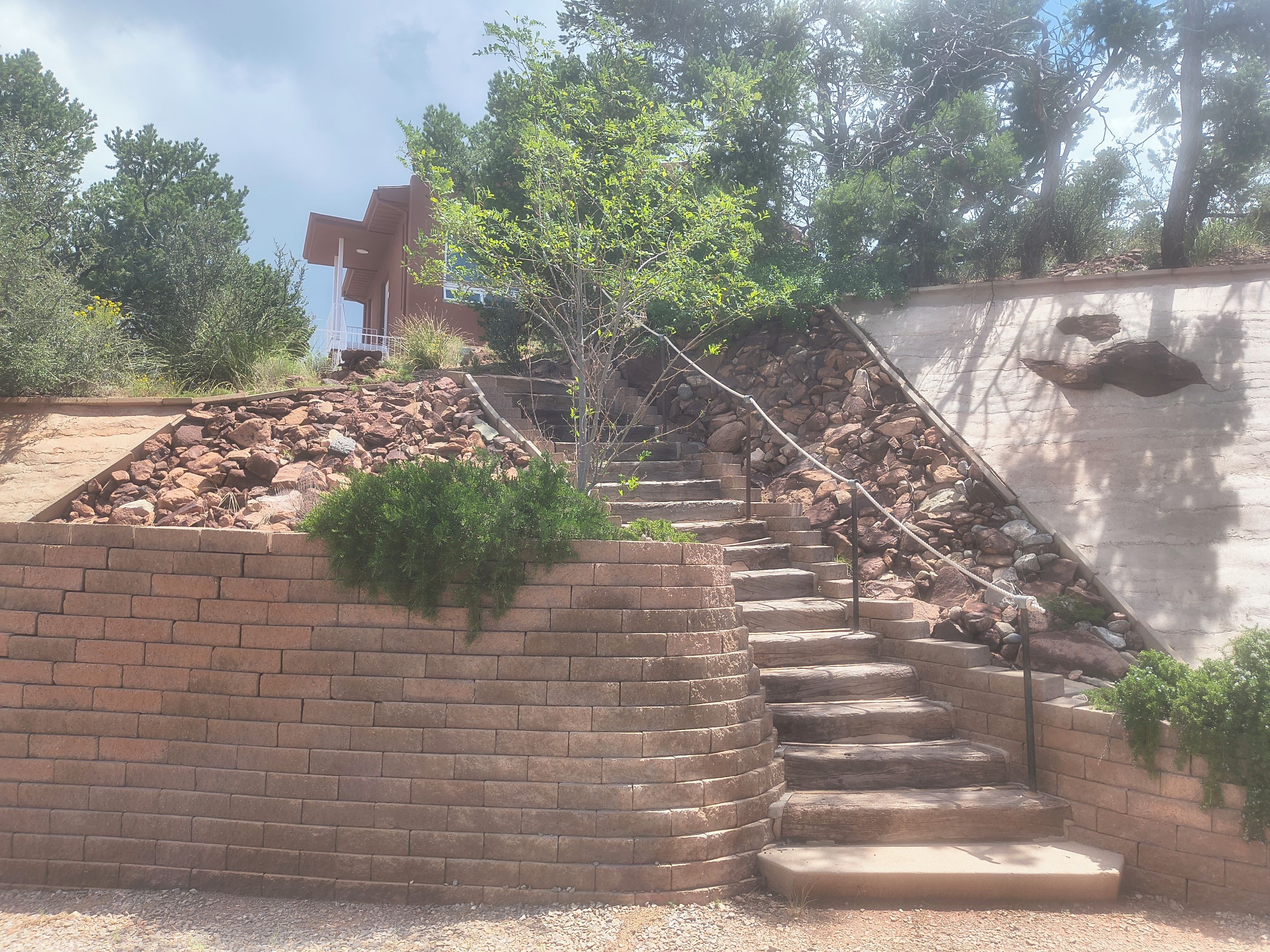 A set of outdoor stone steps leading up to a brick wall, surrounded by greenery and trees.