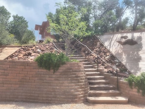 A set of outdoor stone steps leading up to a brick wall, surrounded by greenery and trees.