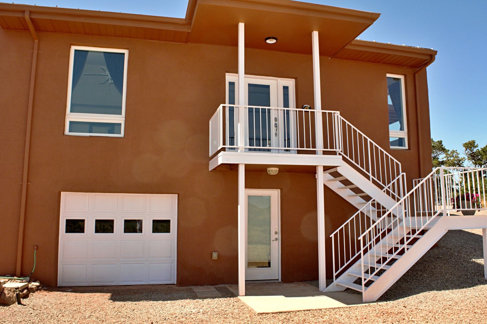 A two-story house with a white garage door, a balcony with a white railing, and a staircase leading to the upper floor.