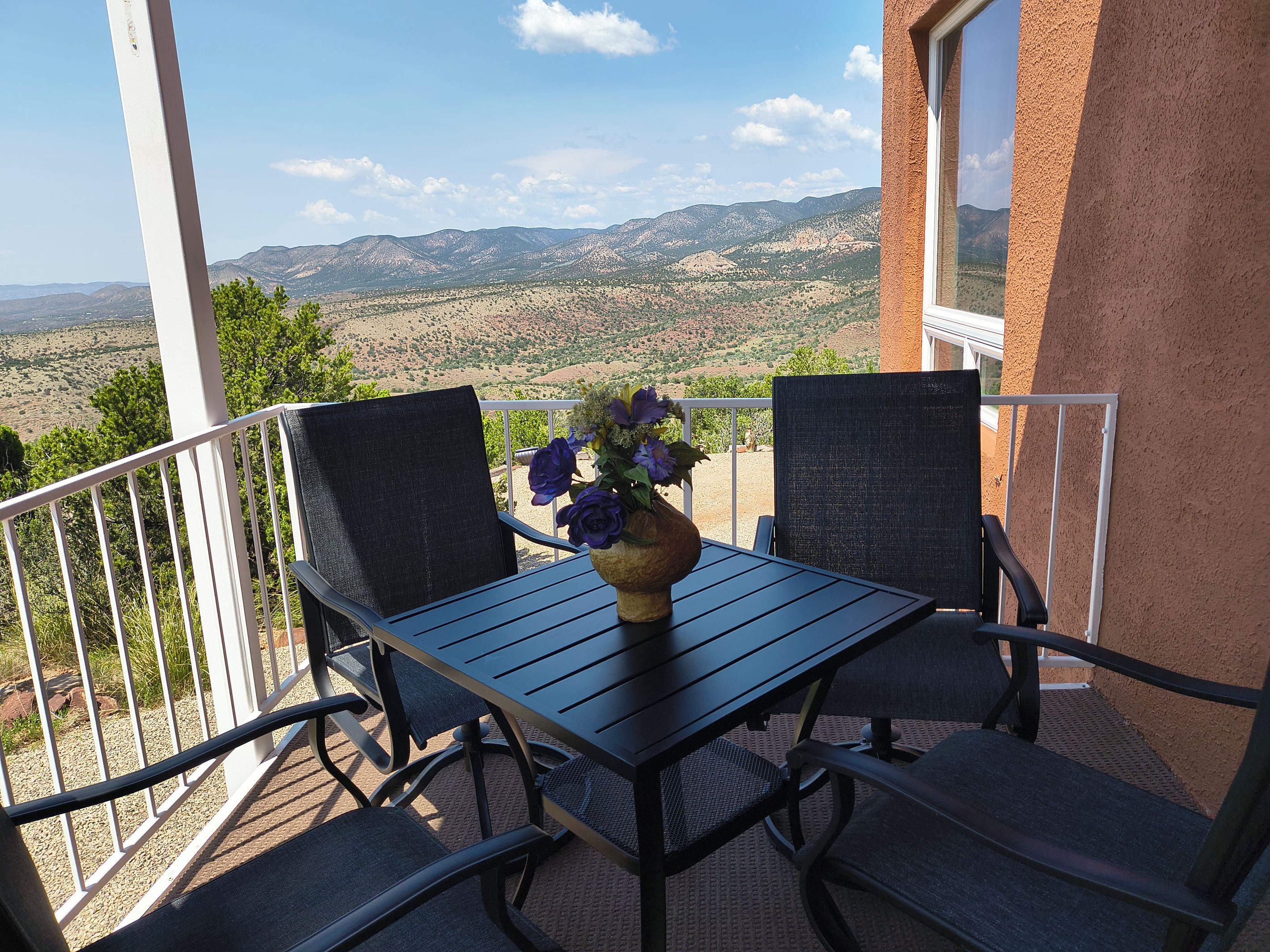 Un balcon avec une table et des chaises, un vase rempli de fleurs et une vue sur les montagnes.