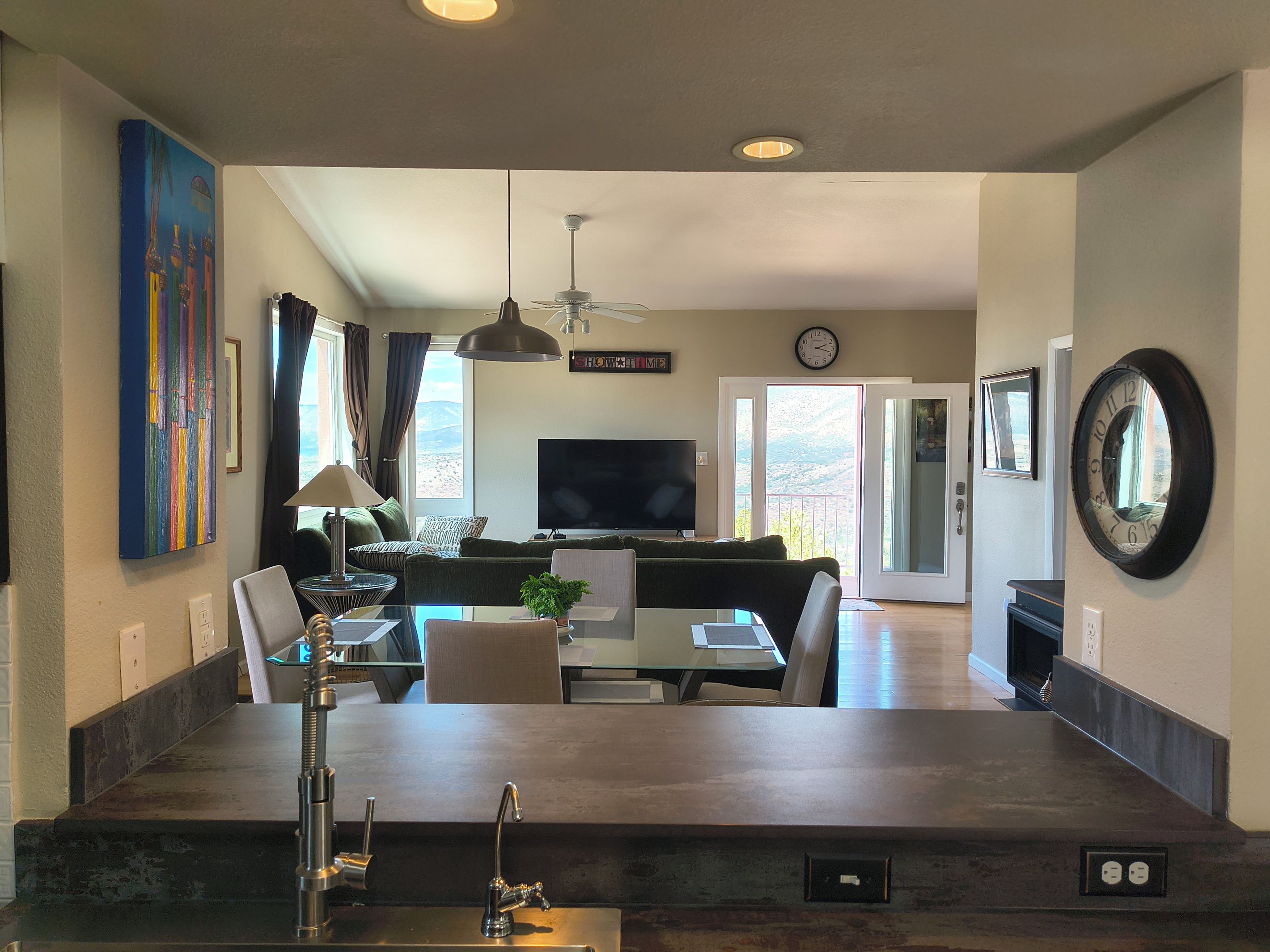 A spacious living area with a sofa, TV, and dining table, a large window with a view, and a kitchen island with a sink.