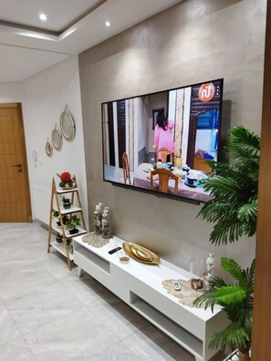 Un salón moderno con un televisor de pantalla plana montado en la pared, un mueble blanco debajo y una puerta de madera a la izquierda.