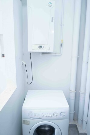 Uma lavanderia compacta com máquina de lavar de abertura frontal e aquecedor de água instalado na parede.