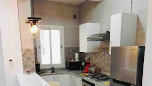 A compact kitchen with a central island, a built-in oven, a refrigerator, and a hanging light fixture.