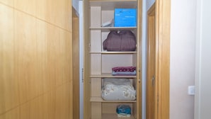 A wooden wardrobe with multiple shelves, a folded blanket, a box, and a package of toilet paper.