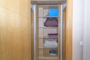 A wooden wardrobe with multiple shelves, a folded blanket, a box, and a package of toilet paper.