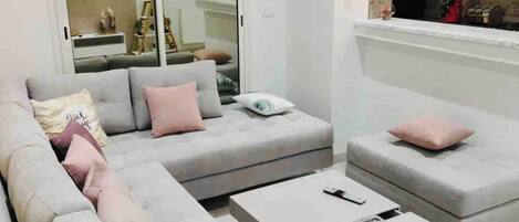 Una sala de estar moderna con un sofá seccional gris, una mesa de centro blanca y una mesita auxiliar blanca.