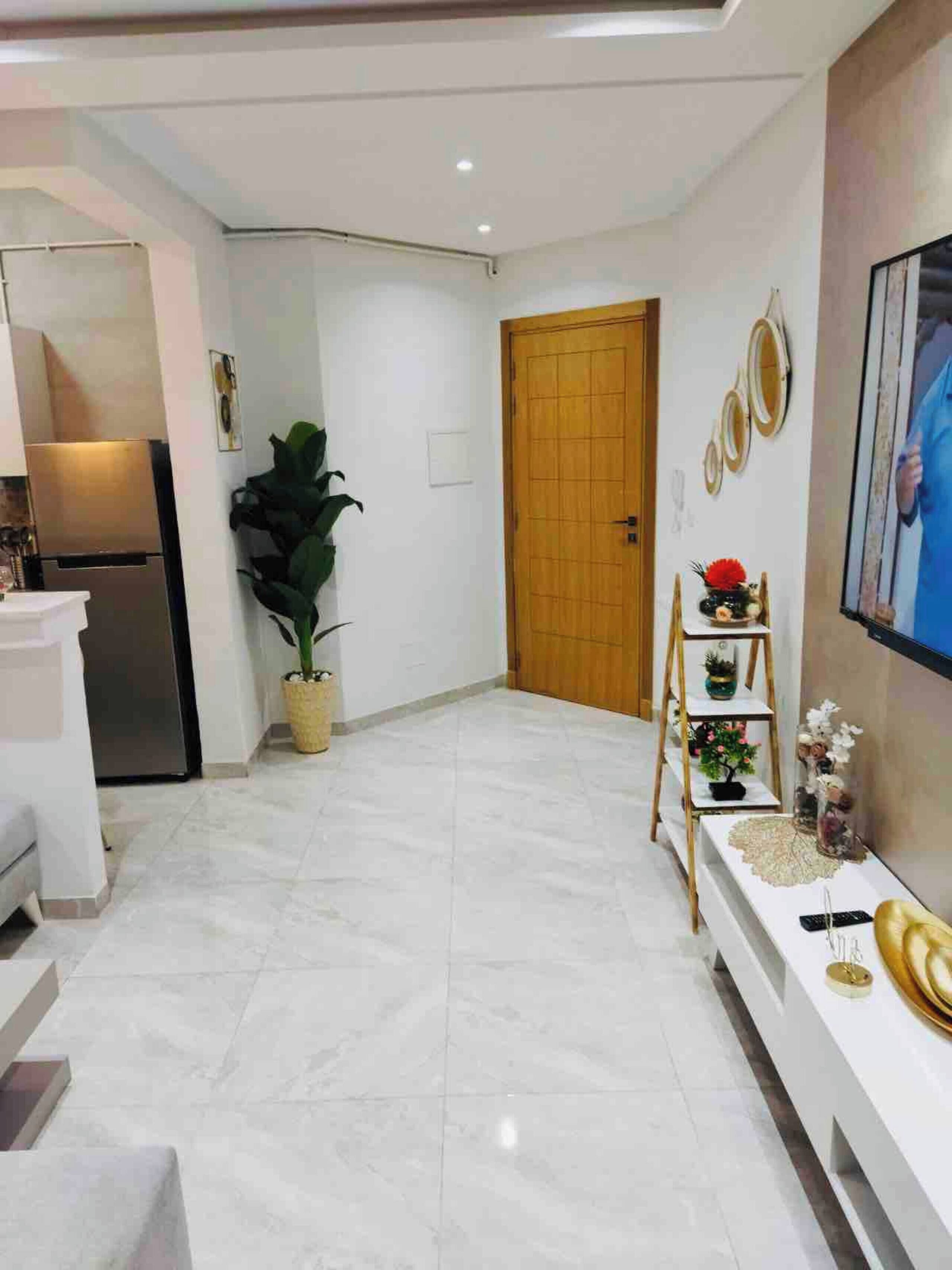 Uma sala de estar moderna com um sofá branco, uma porta de madeira e uma TV fixada na parede.