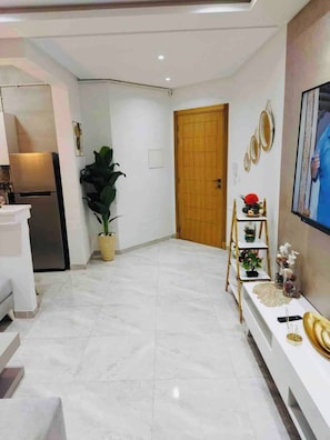 A modern living room with a white sofa, a wooden door, and a TV mounted on the wall.