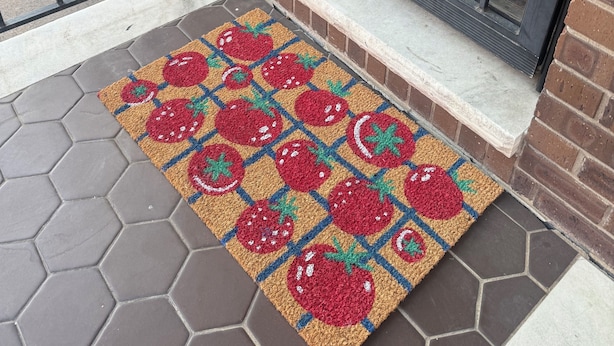 A red brick building with a metal gate and a colorful doormat with a tomato pattern.