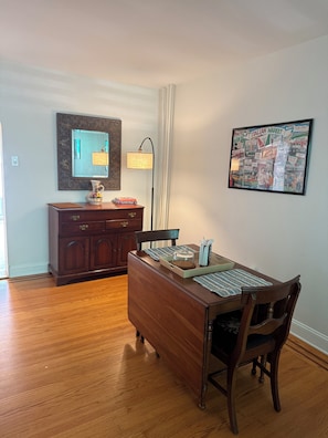 A dining area with a wooden table, chairs, a mirror, and a framed picture on the wall.