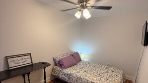A bedroom with a bed, a nightstand, a ceiling fan, and a wall-mounted TV.