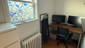 A room with a desk, two monitors, a radiator, and a window with a floral pattern.