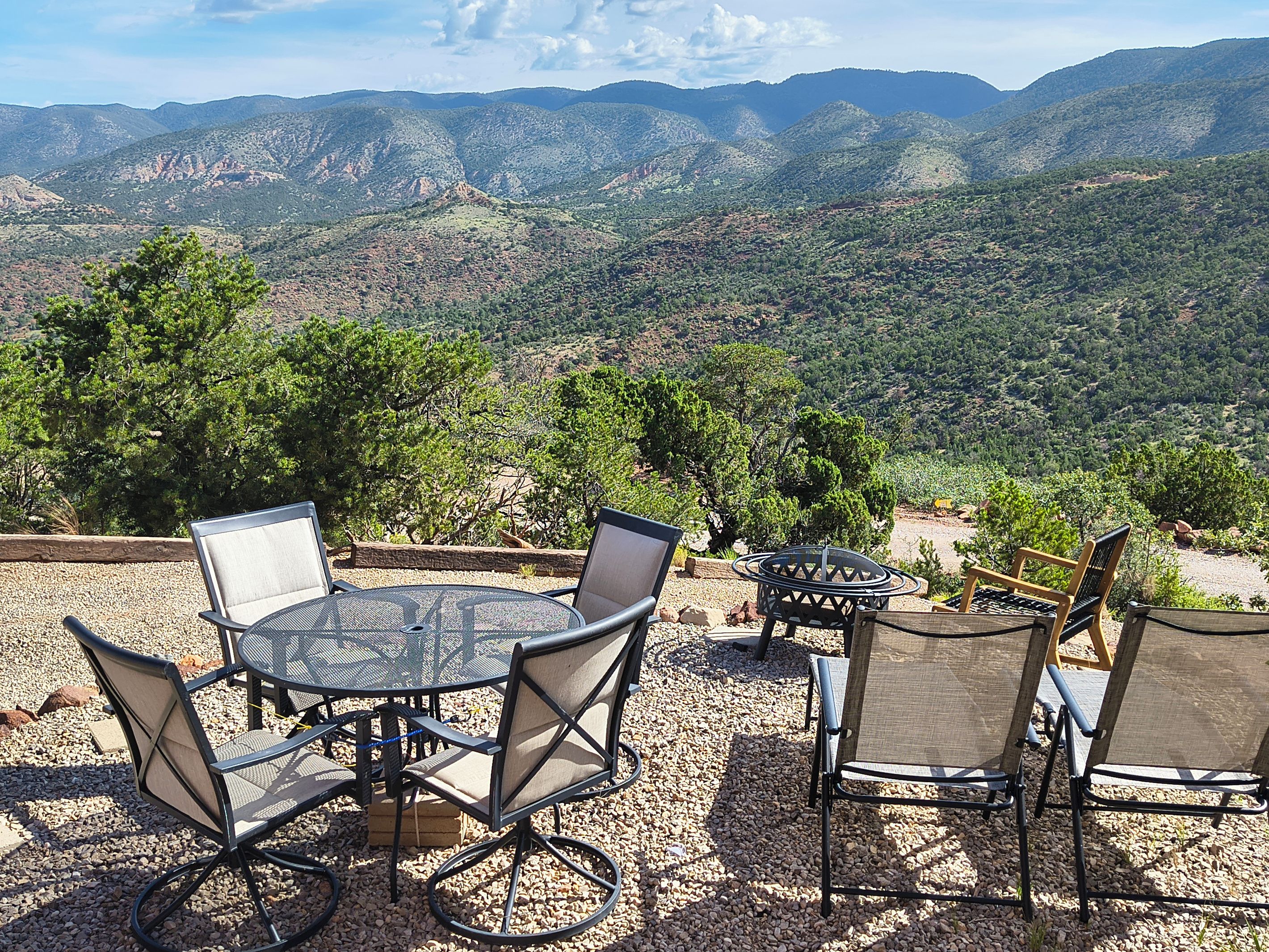 An outdoor seating area with a round table and chairs, surrounded by gravel, overlooking a mountainous landscape.
