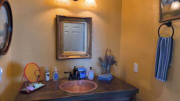 A bathroom with a wooden vanity, a mirror, wall-mounted lights, a towel rack, and a framed picture.