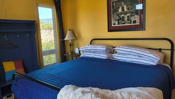 A hotel room with a bed, a nightstand, a lamp, a framed picture on the wall, and a view of the outdoors.