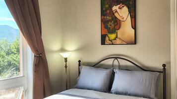 A bedroom with a bed, a painting on the wall, a lamp, and a window with curtains.