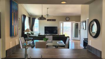 A spacious living area with a sofa, TV, and dining table, a large window with a view, and a kitchen island with a sink.